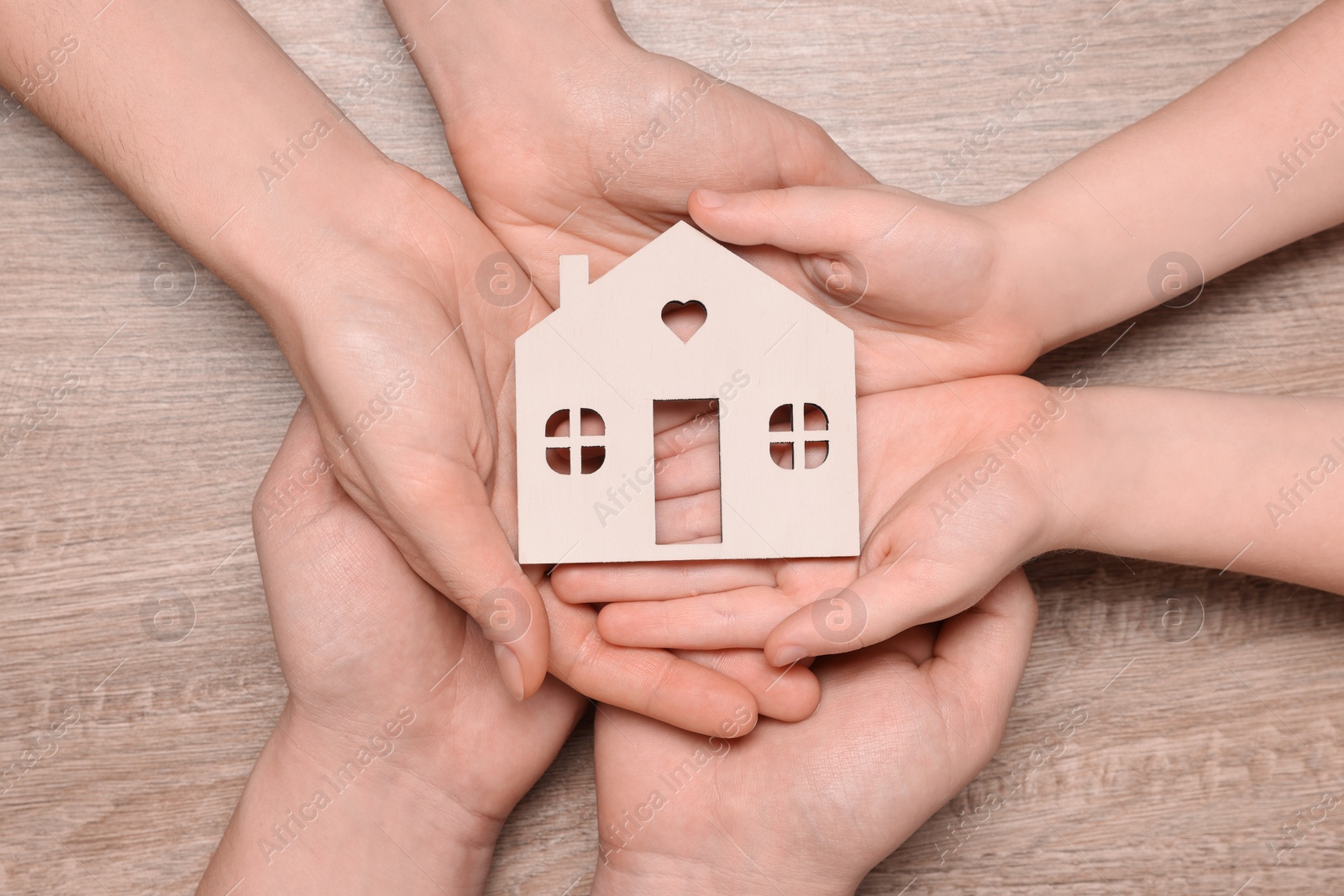 Photo of Home security concept. Family holding house model at wooden table, top view