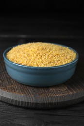 Photo of Bowl of uncooked bulgur on black wooden table