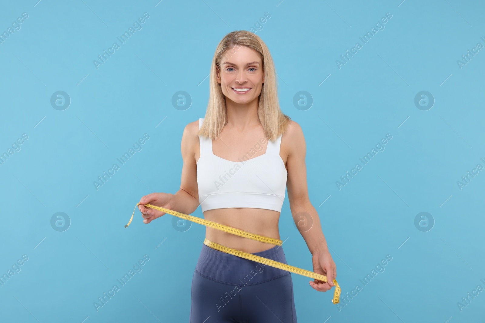 Photo of Slim woman measuring waist with tape on light blue background. Weight loss