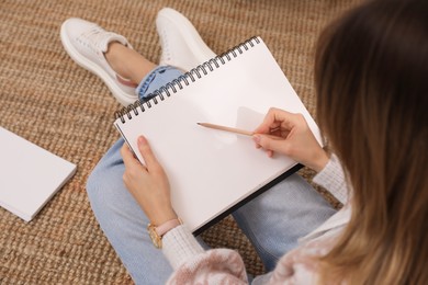 Photo of Woman drawing in sketchbook with pencil on floor at home, above view