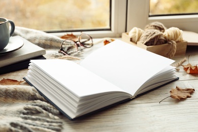 Photo of Open book and autumn leaves on windowsill. Space for text