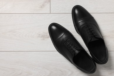 Photo of Pair of black leather men shoes on light wooden floor, top view. Space for text