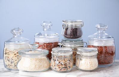 Photo of Brown and polished rice in jars on white marble table