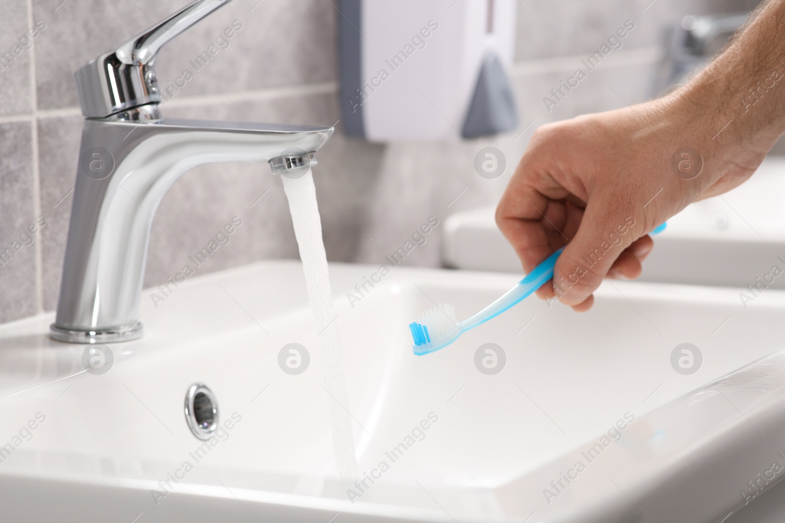 Photo of Man holding toothbrush near flowing water above sink in bathroom, closeup