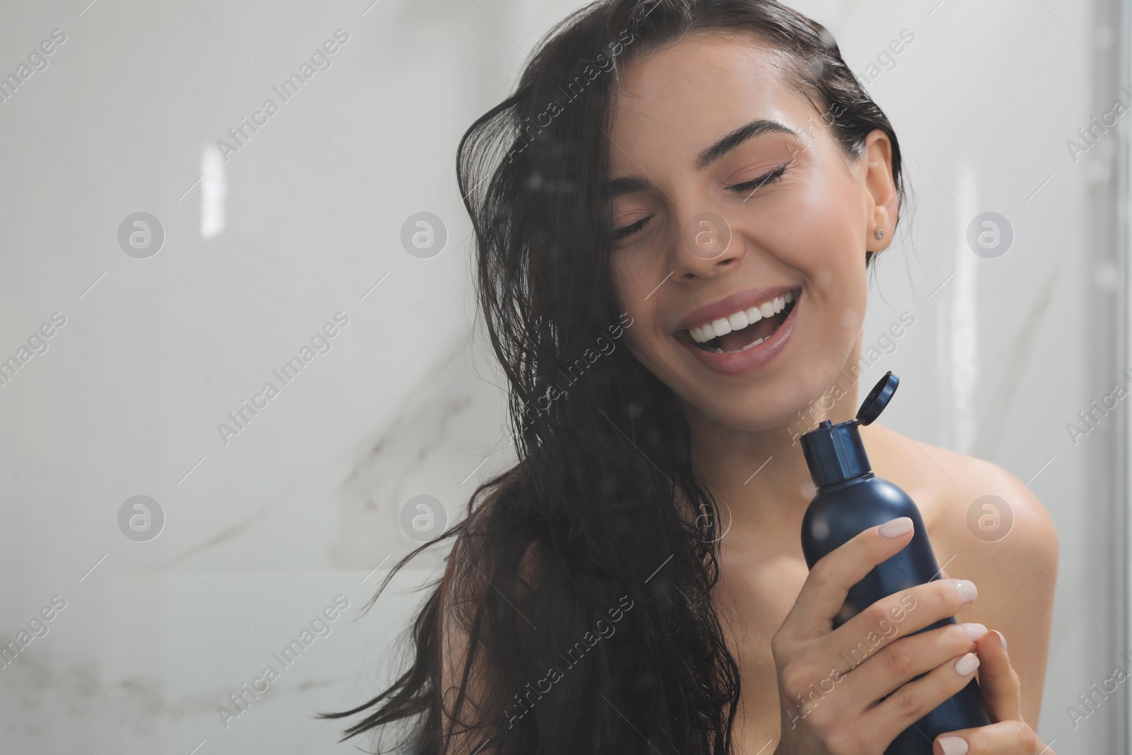 Photo of Young woman with bottle of gel singing while taking shower, view through glass