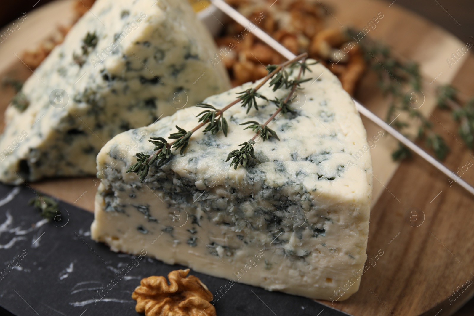 Photo of Tasty blue cheese with thyme on wooden board, closeup