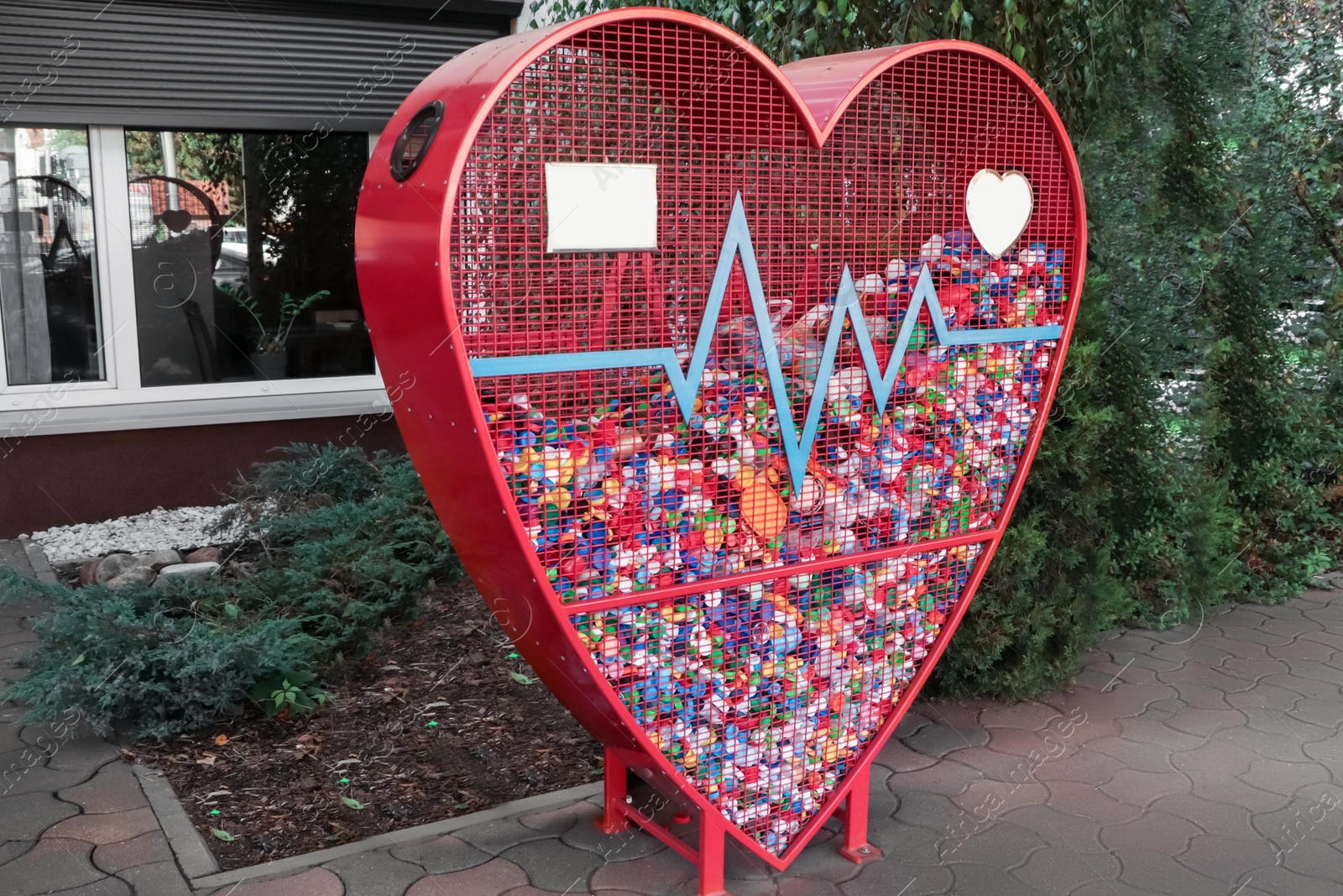 Photo of Heart shaped red recycling container for plastic caps outdoors