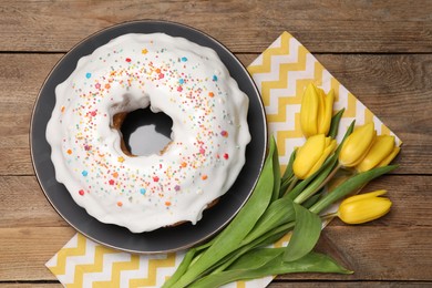 Easter cake with sprinkles and tulips on wooden table, flat lay