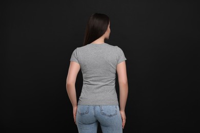 Woman wearing grey t-shirt on black background, back view