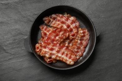 Photo of Fried bacon slices on dark textured table, top view