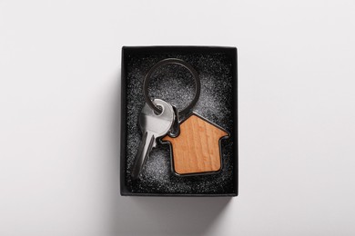 Key with trinket in shape of house and gift box on light grey background, top view. Housewarming party
