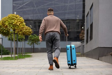 Being late. Man with light blue suitcase walking outdoors, back view
