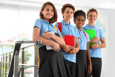 Photo of Happy pupils in school uniform with backpacks indoors