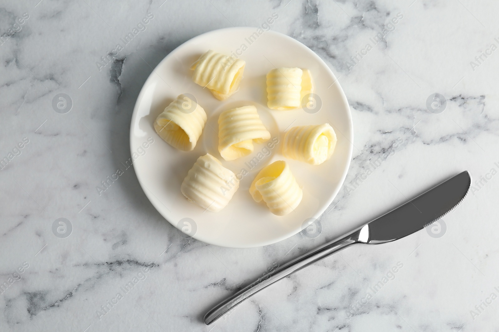 Photo of Plate with butter curls and knife on table, top view