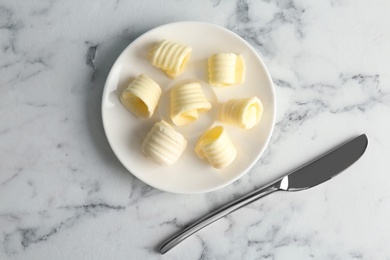 Plate with butter curls and knife on table, top view