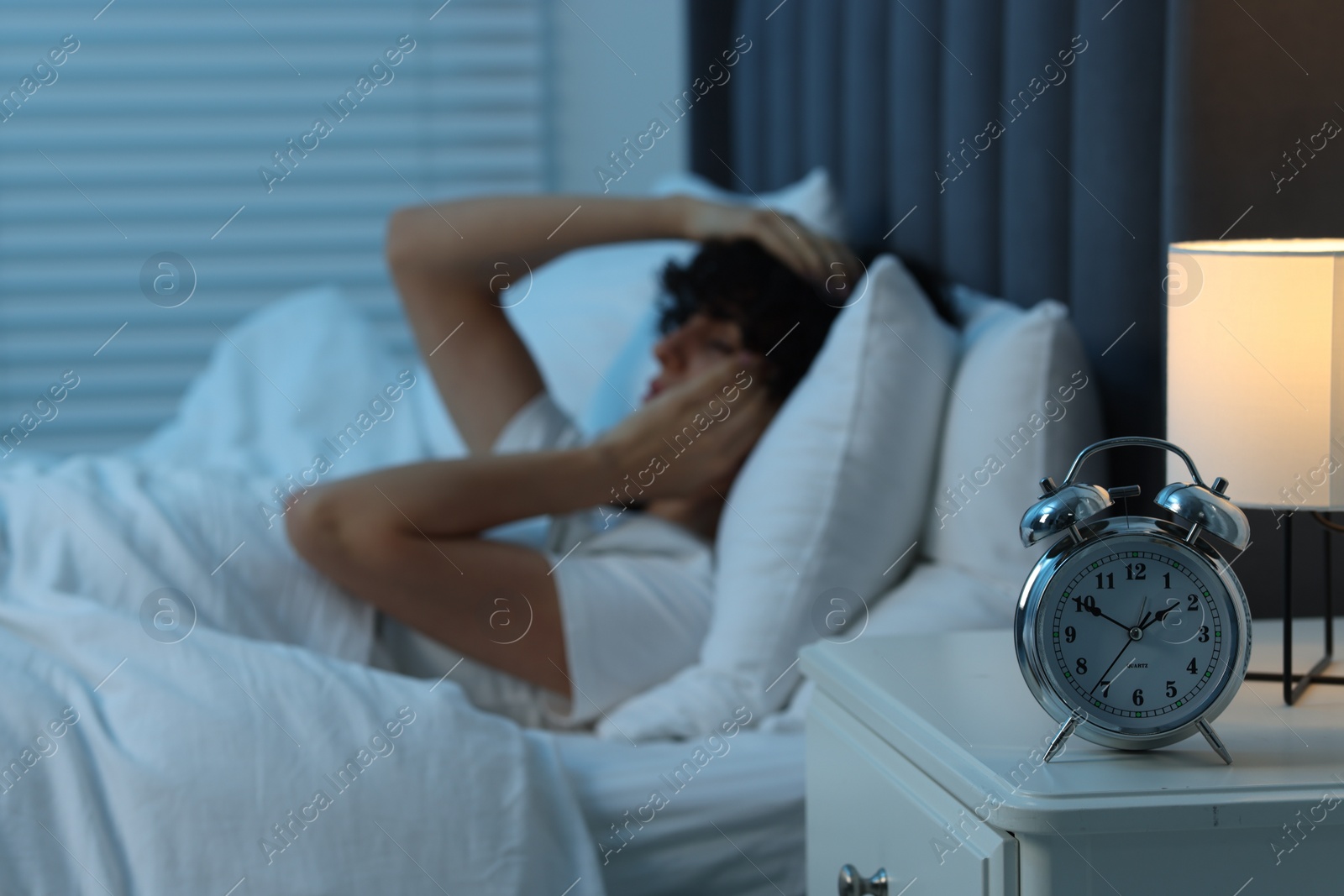 Photo of Young woman suffering from headache in bed at night, focus on alarm clock