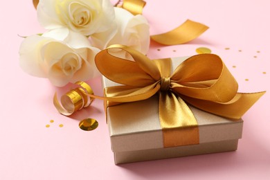Photo of Beautiful golden gift box, flowers and confetti on pink background