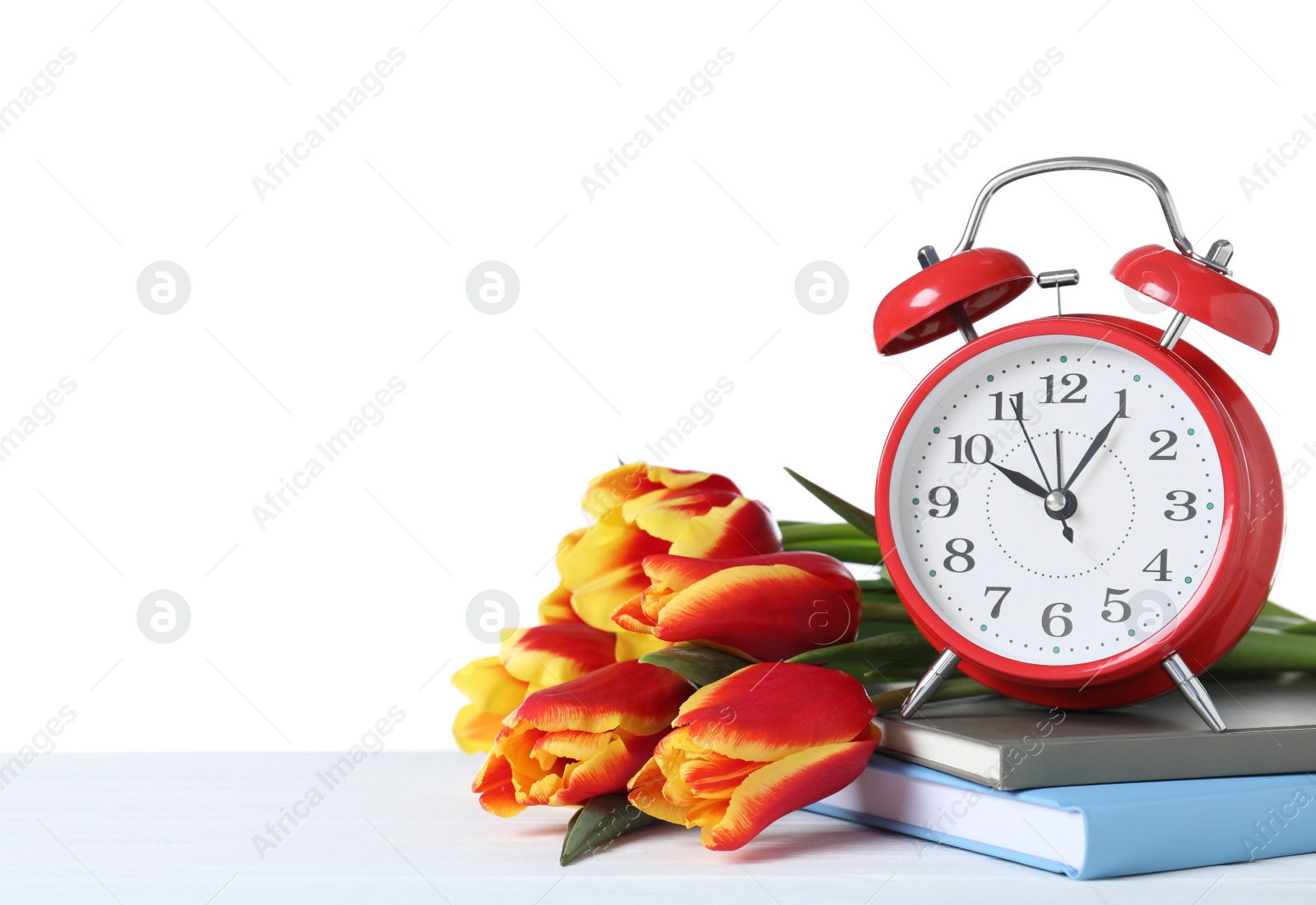 Photo of Red alarm clock, books and spring flowers on wooden table against white background, space for text. Time change