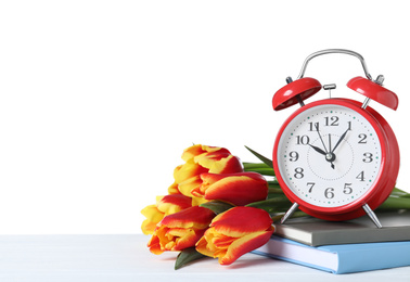 Photo of Red alarm clock, books and spring flowers on wooden table against white background, space for text. Time change