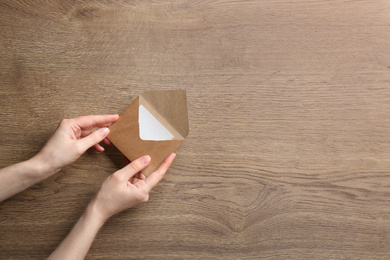 Photo of Woman holding brown paper envelope on wooden background, closeup. Space for text
