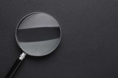 Photo of Magnifying glass on dark background, top view. Space for text