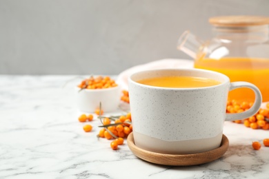 Photo of Delicious sea buckthorn tea and fresh berries on white marble table. Space for text
