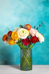 Photo of Vase with beautiful ranunculus flowers on table against color background, space for text
