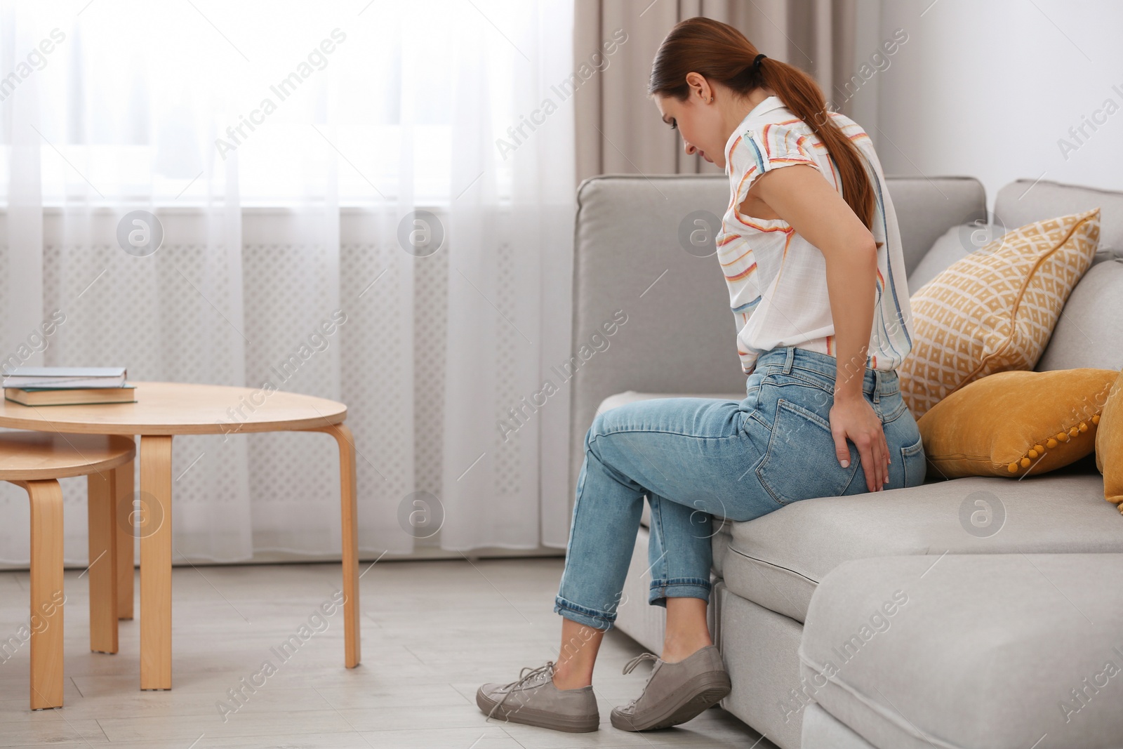 Photo of Young woman suffering from hemorrhoid on sofa at home