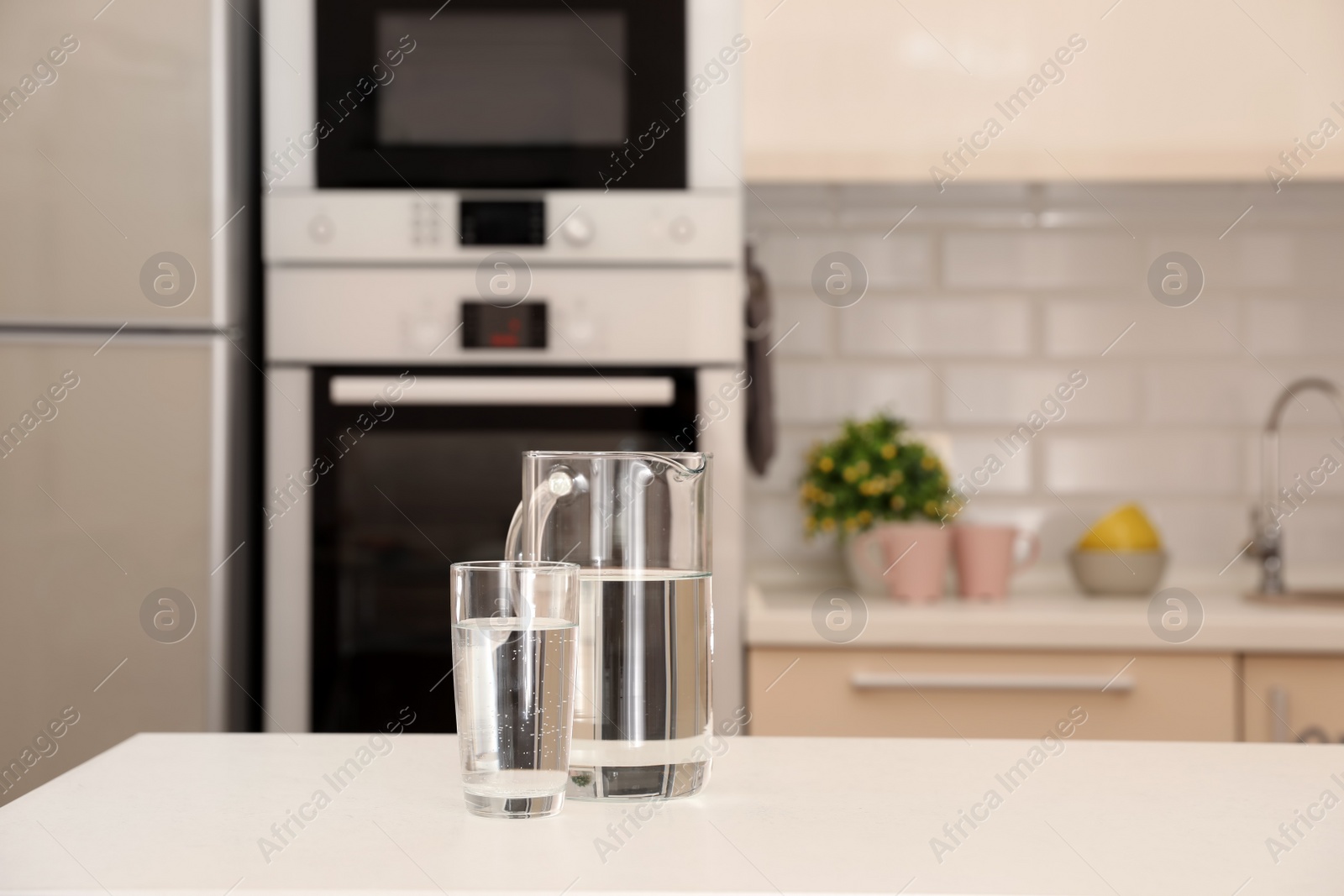 Photo of Jug and glass with water on table in kitchen. Space for text