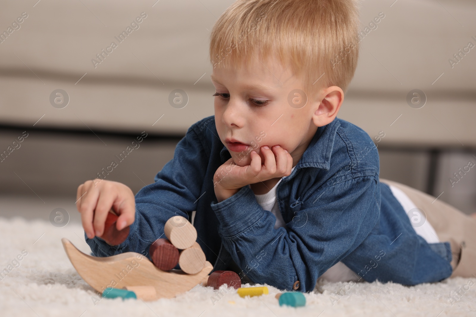 Photo of Cute little boy playing with wooden balance toy on carpet indoors