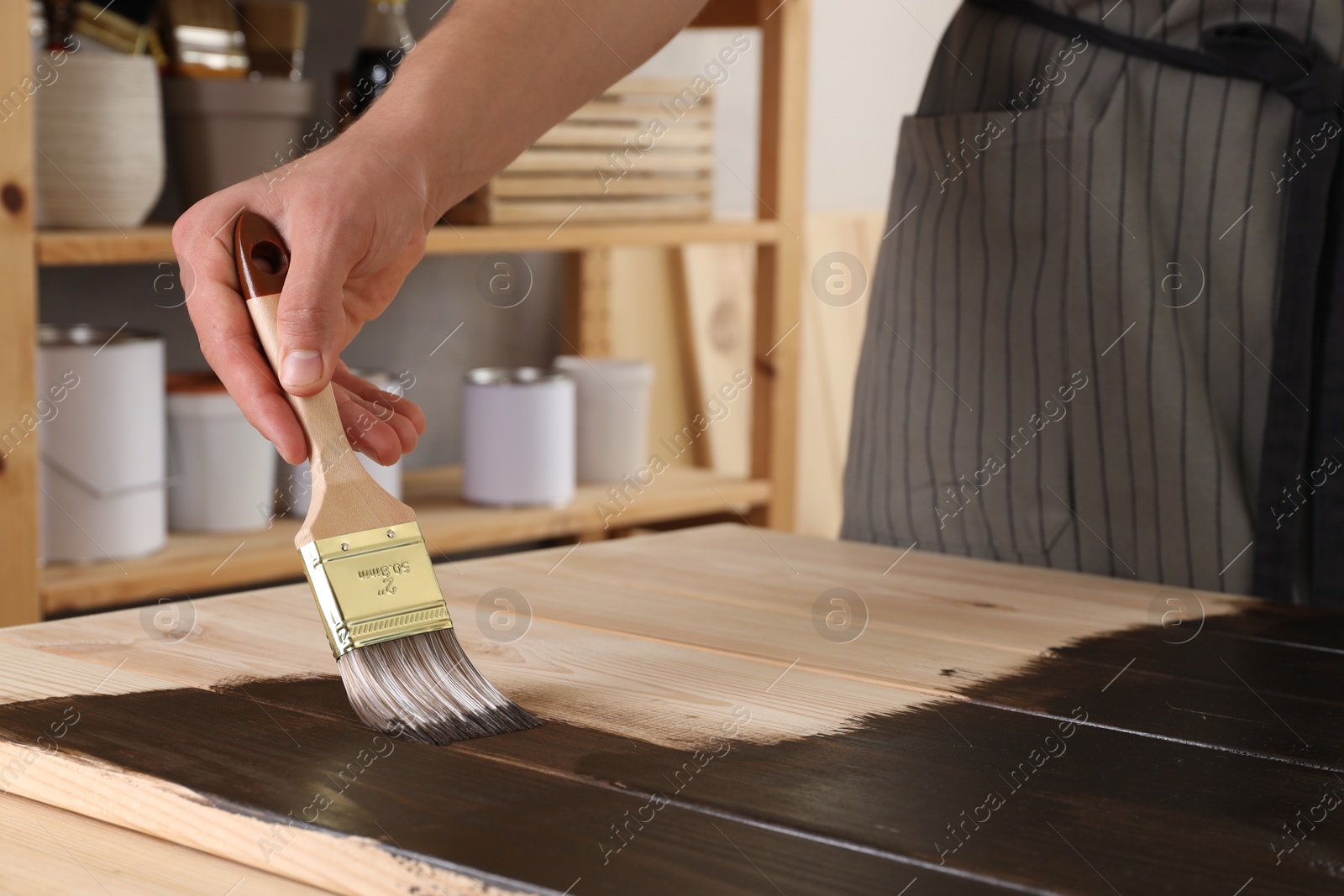 Photo of Man with brush applying wood stain onto wooden surface indoors, closeup