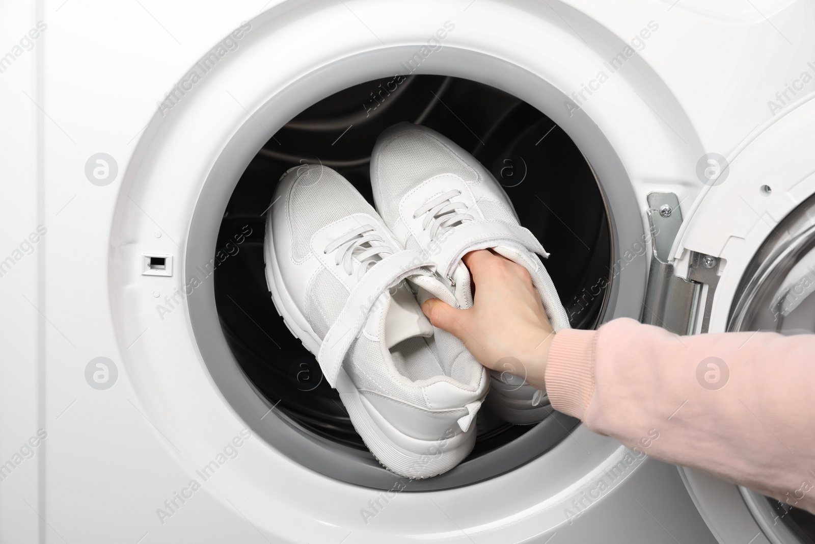 Photo of Woman putting stylish sneakers into washing machine, closeup