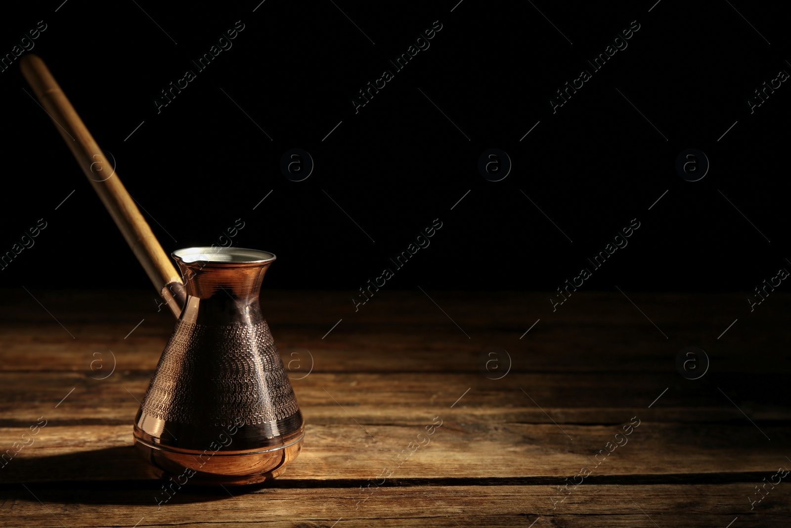 Photo of Beautiful copper turkish coffee pot on wooden table against dark background, space for text