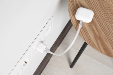 Photo of Modern wireless earphones charging from electric socket indoors, above view