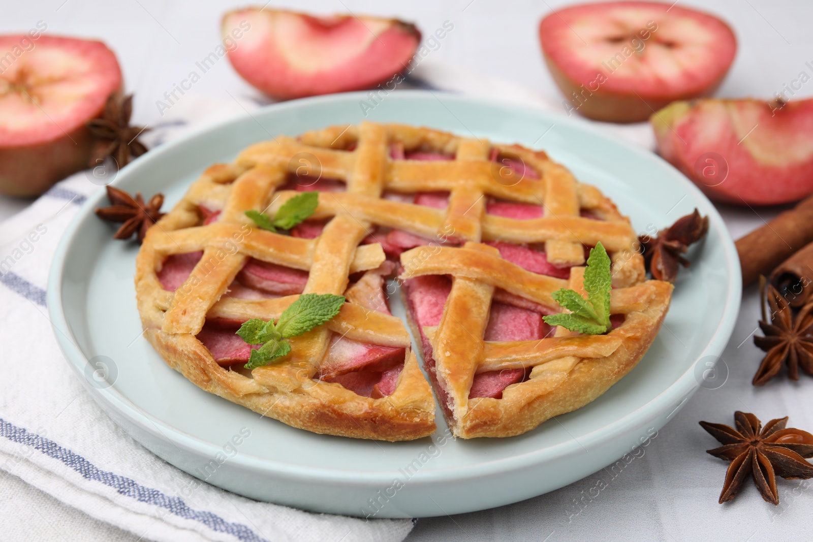Photo of Delicious apple pie with mint and ingredients on white tiled table, closeup