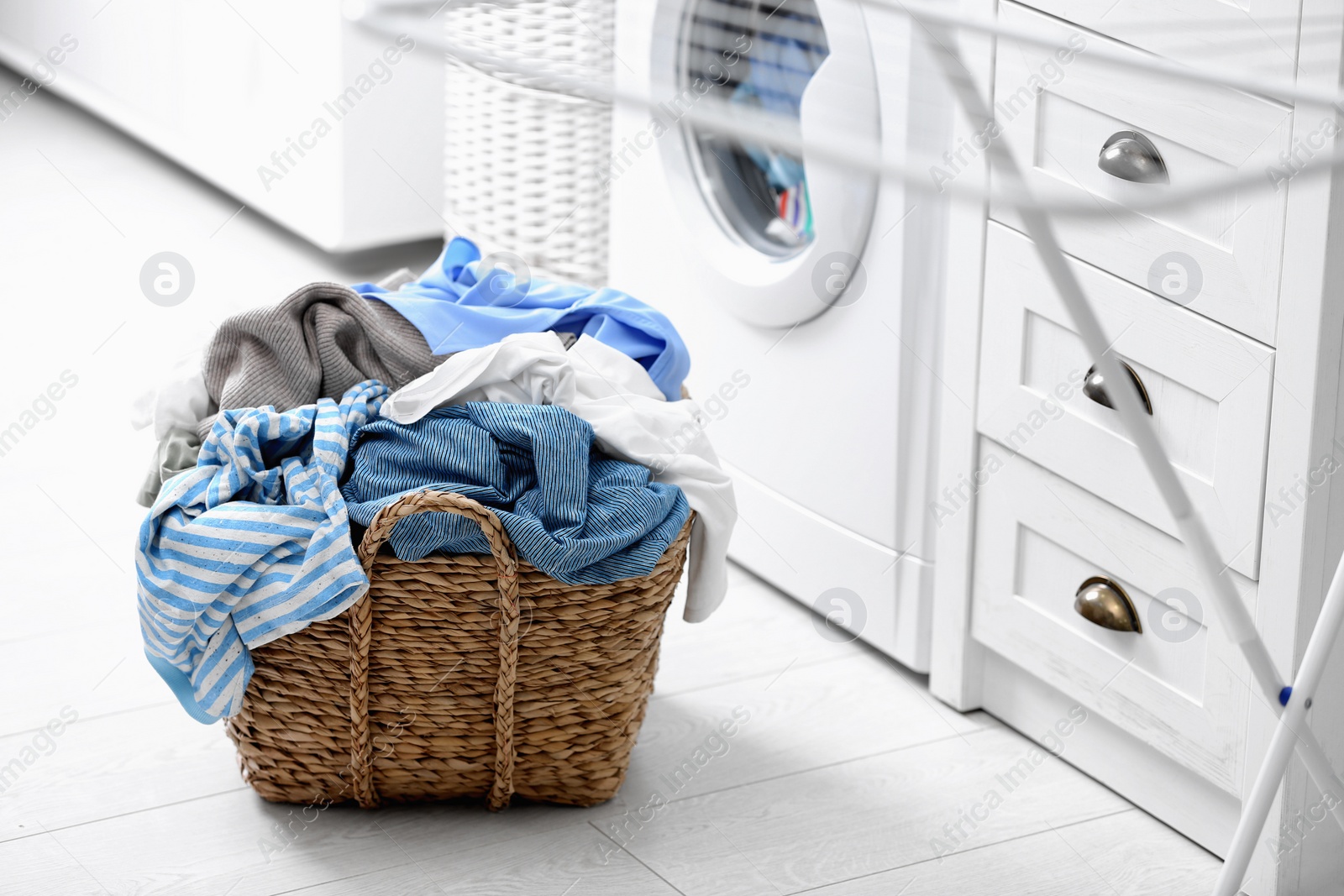 Photo of Wicker basket with dirty laundry on floor indoors