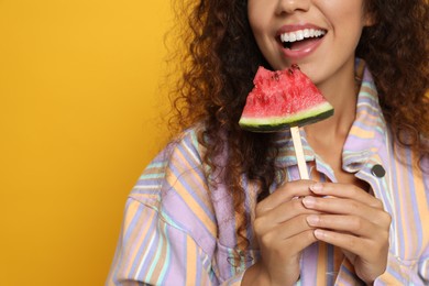 Photo of Beautiful young African American woman with piece of watermelon on yellow background, closeup. Space for text