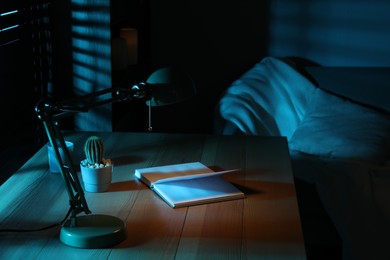 Stylish lamp and open book on wooden table at night