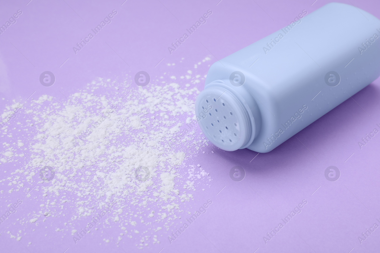 Photo of Bottle and scattered dusting powder on violet background, space for text. Baby cosmetic product
