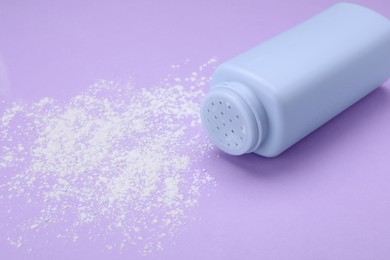 Bottle and scattered dusting powder on violet background, space for text. Baby cosmetic product