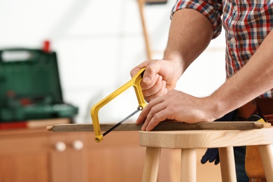 Photo of Man working with hand saw indoors, closeup. Home repair