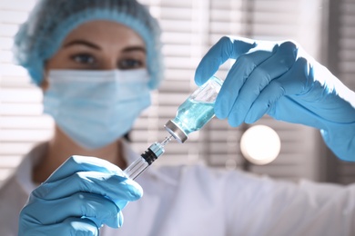 Woman filling syringe with vaccine from vial against blurred background, focus on hands