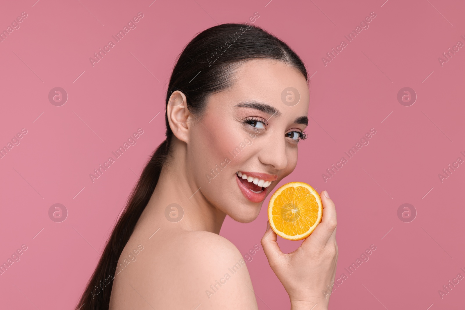 Photo of Beautiful young woman with piece of orange on pink background