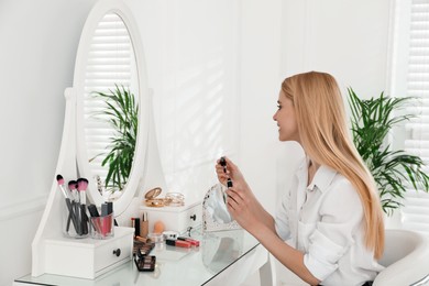 Beautiful woman applying makeup near mirror in room