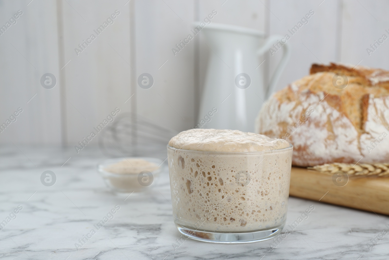 Photo of Glass jar with sourdough on white marble table. Space for text