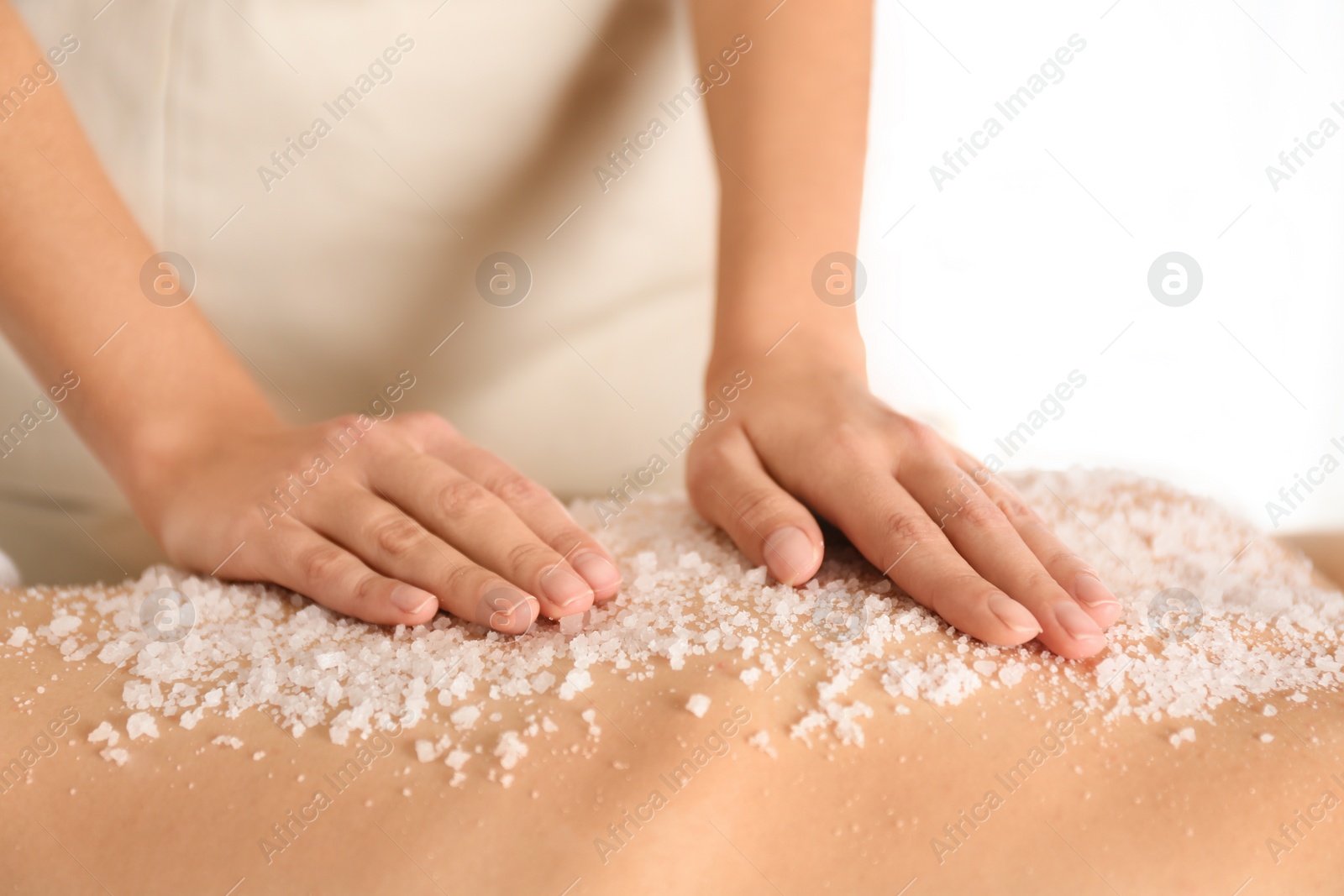 Photo of Young woman having body scrubbing procedure with sea salt in spa salon, closeup