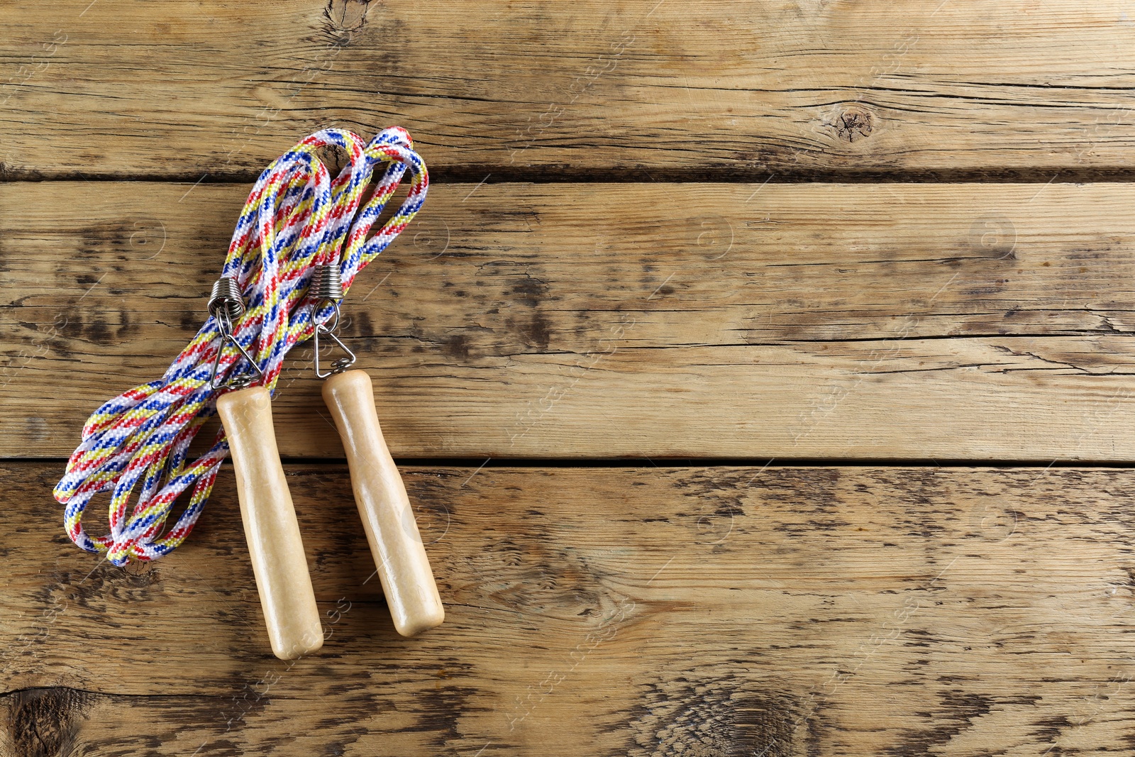 Photo of Skipping rope on wooden table, top view. Space for text