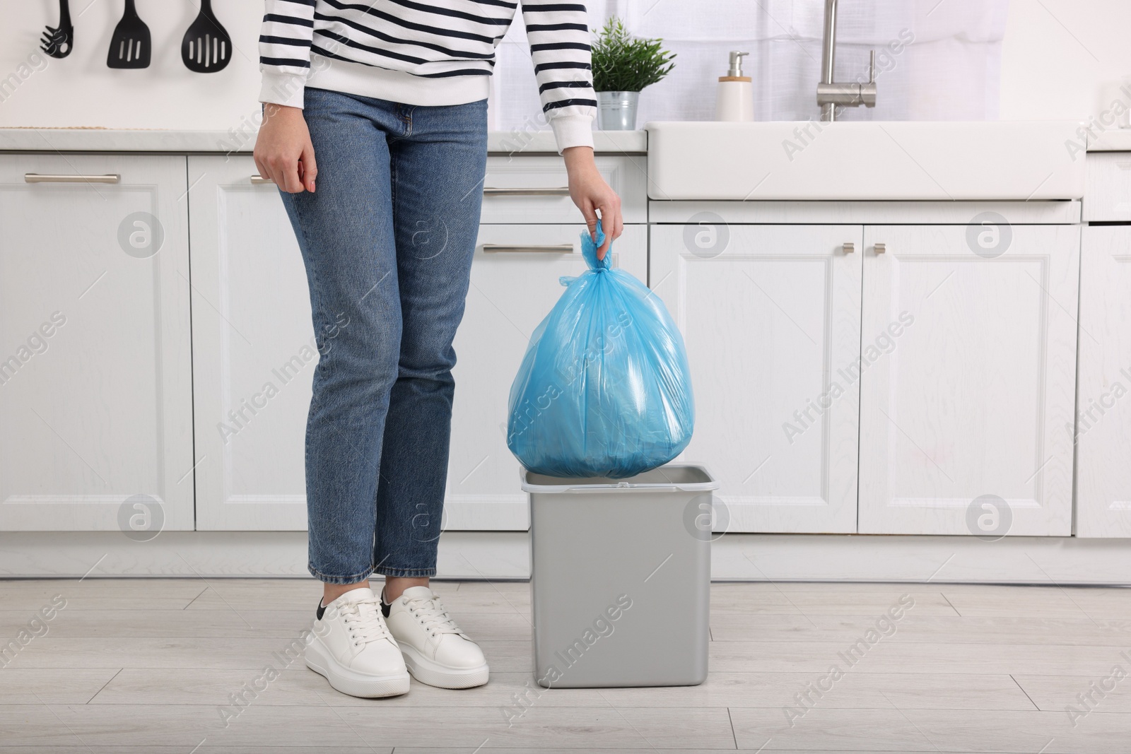 Photo of Woman taking garbage bag out of trash bin in kitchen, closeup. Space for text