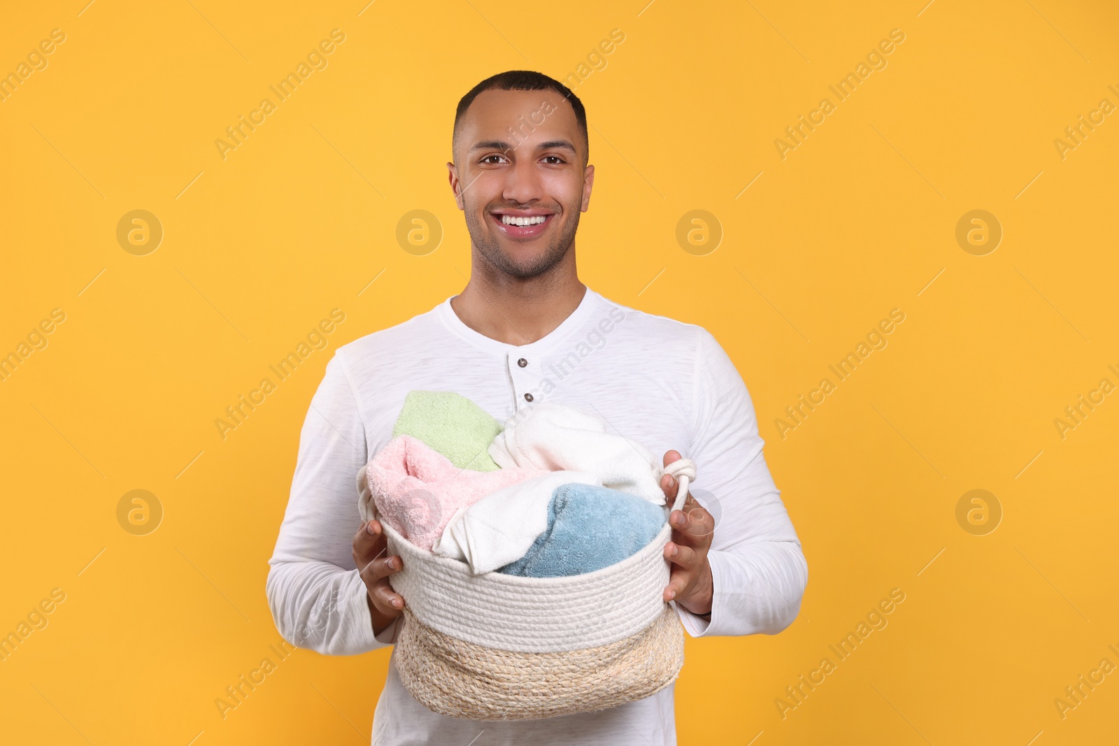 Photo of Happy man with basket full of laundry on orange background