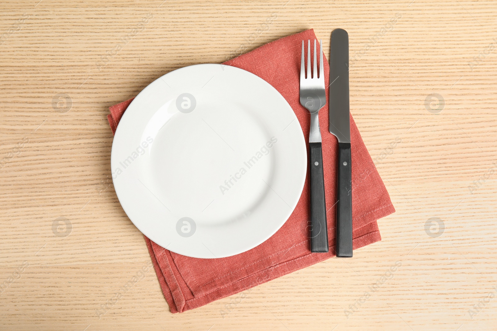 Photo of Empty white ceramic plate, towel and cutlery on wooden table, flat lay